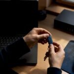 Mani che tengono un token di sicurezza posato su una scrivania in un ufficio IT